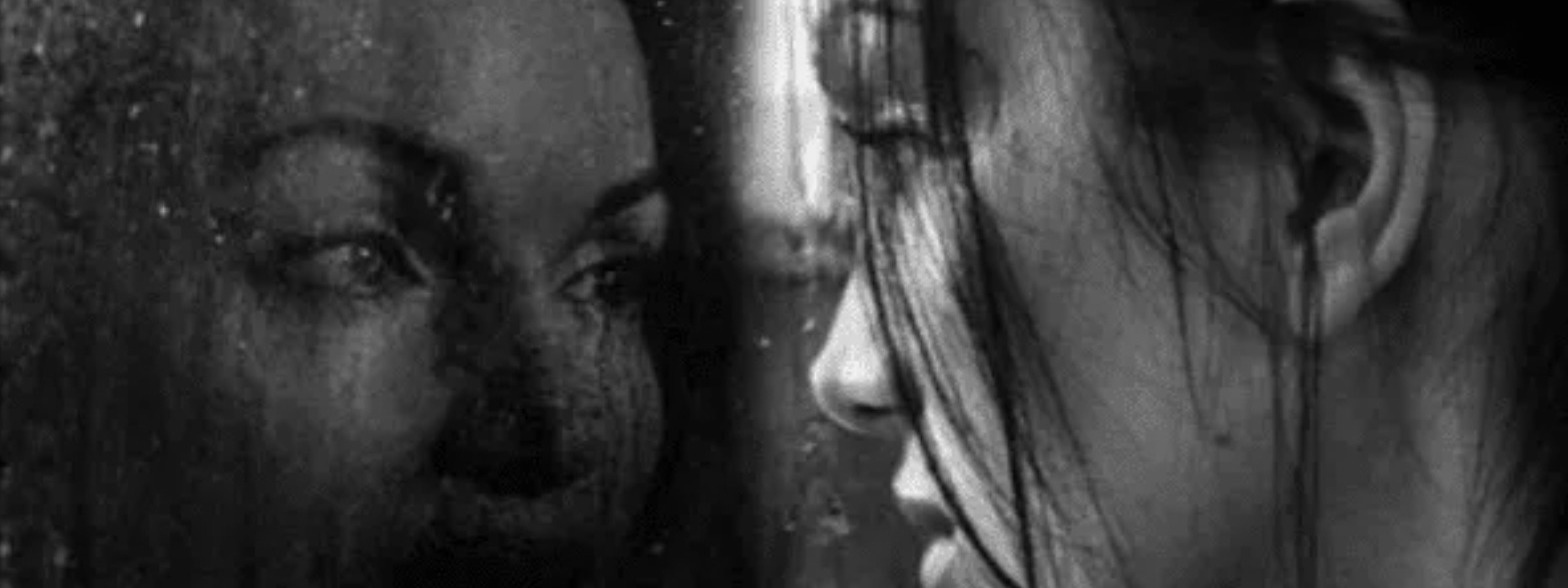 A Black And White Photograph of A Woman Looking At Herself In A Mirror With Rain Drops Running Down
